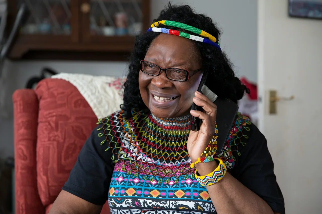 An older woman in a beaded headband smiling as she talks on her mobile phone