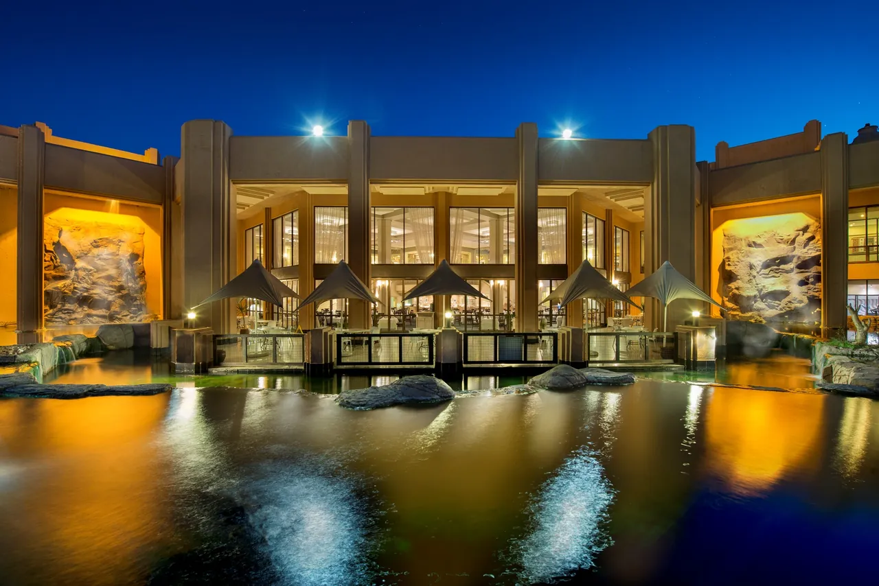 The floodlit main building of the resort reflected in water at night